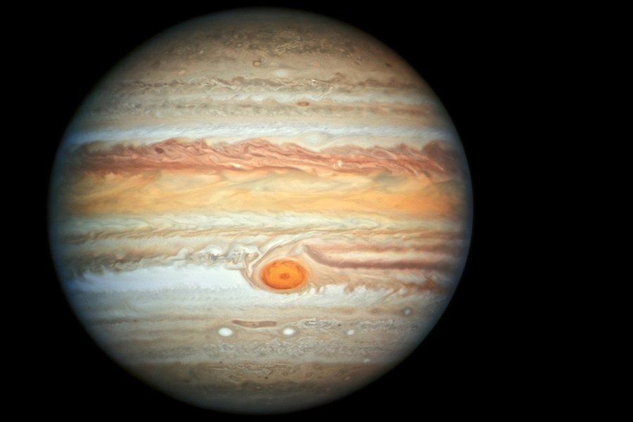 Jupiter med sina karaktäristiska horisontella linjer i rött och orange. I nedre delen av mitten en fläck liknade ett öga. Svart bakgrund.