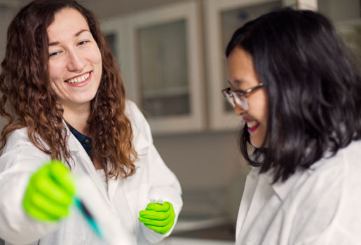 Två kvinnliga forskare i vita rockar i laboratoriemiljö.