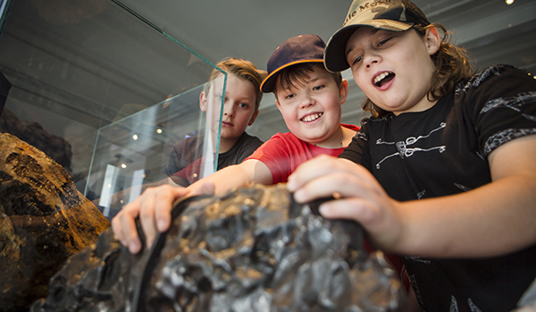 Två pojkar håller i den stora meteoriten i utställningen Skatter från jordens inre.