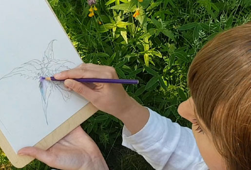 En person sitter utomhus och tecknar en blomma med akvarellpennor.