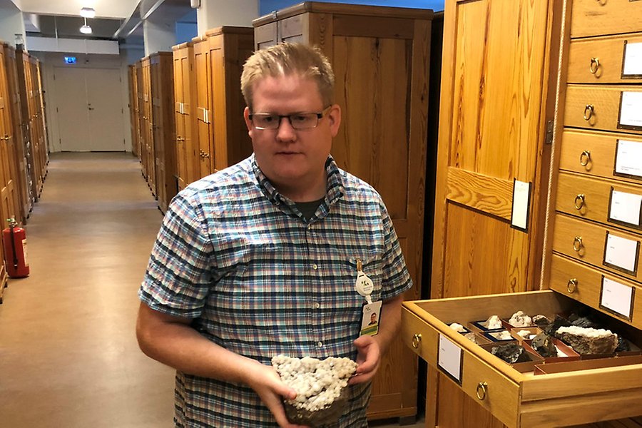 Andreas Karlsson, jourhavande geolog, står framför ett skåp med lådor med samlingsföremål från geologiska enheten, många små prover med tillhörande etiketter.