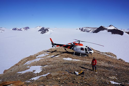Forskare framför helikopter på bergstopp i Antarktis